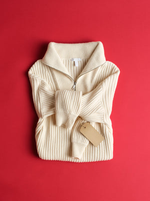Folded cream ribbed sweater with a tag on a red background. 