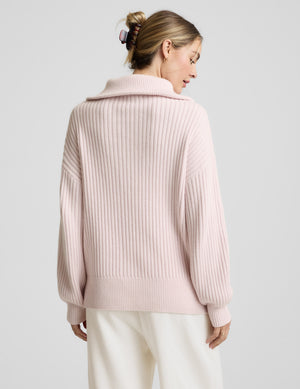 Woman wearing a light pink quarter zip sweater and white fleece pants against a plain background. 