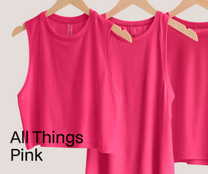 Three pink tank tops hanging on wooden hangers with 'All Things Pink' text.
